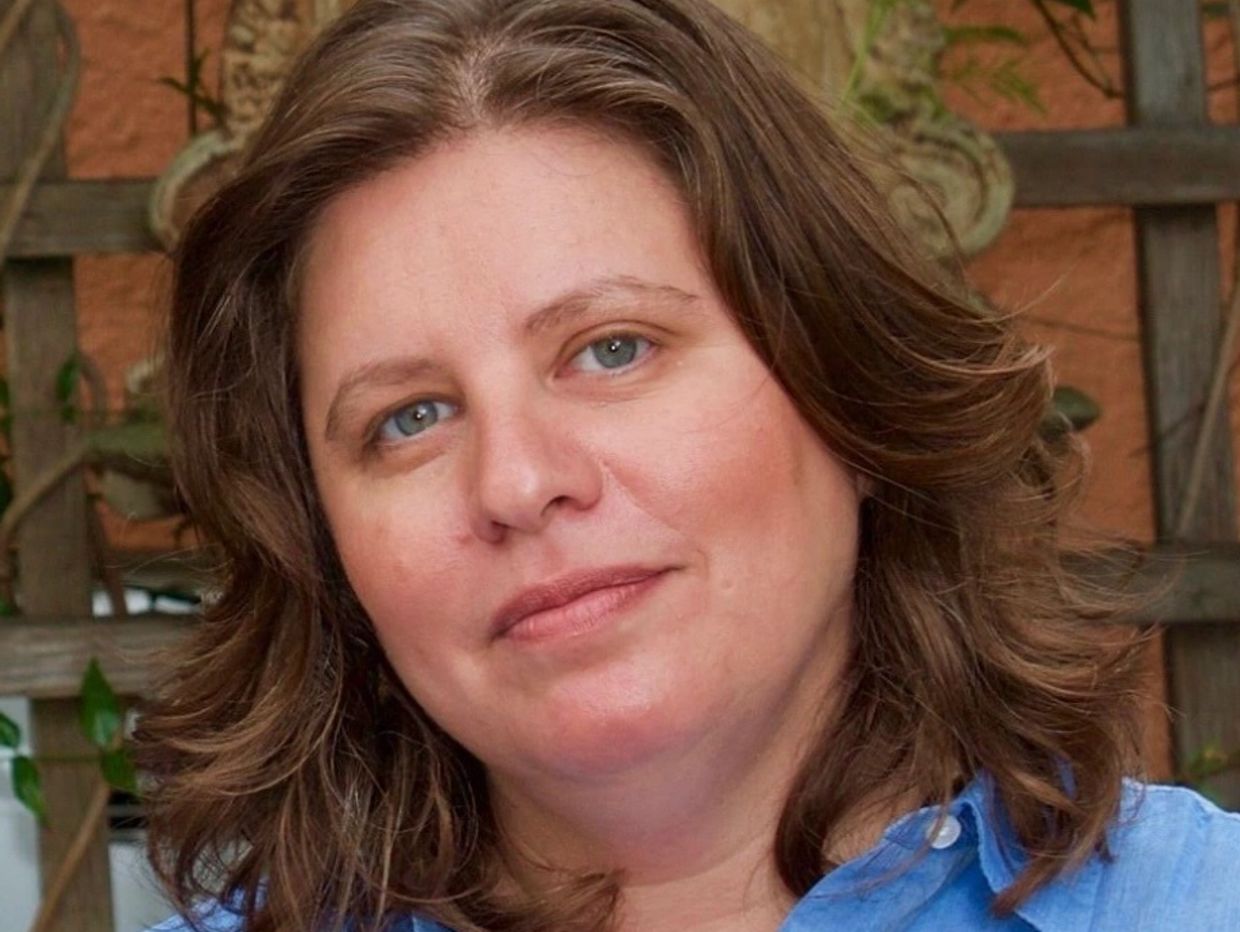 Woman with blue eyes and wavy brown hair smiling gently.