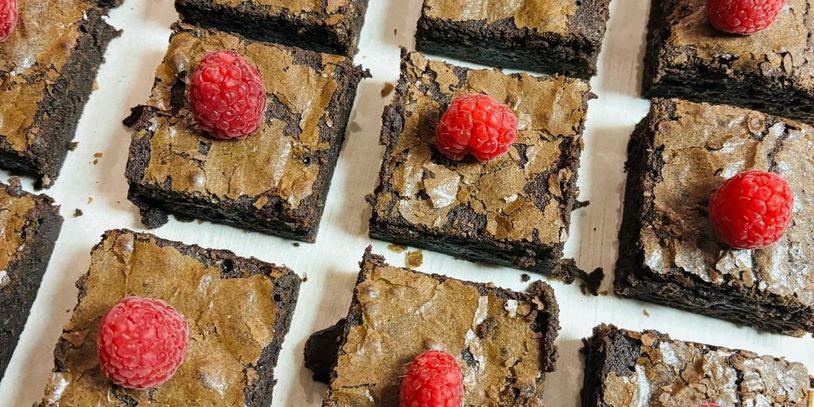 Chocolate brownies topped with fresh raspberries arranged on a white surface.