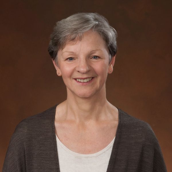 Smiling mature woman with short gray hair against a brown background.
