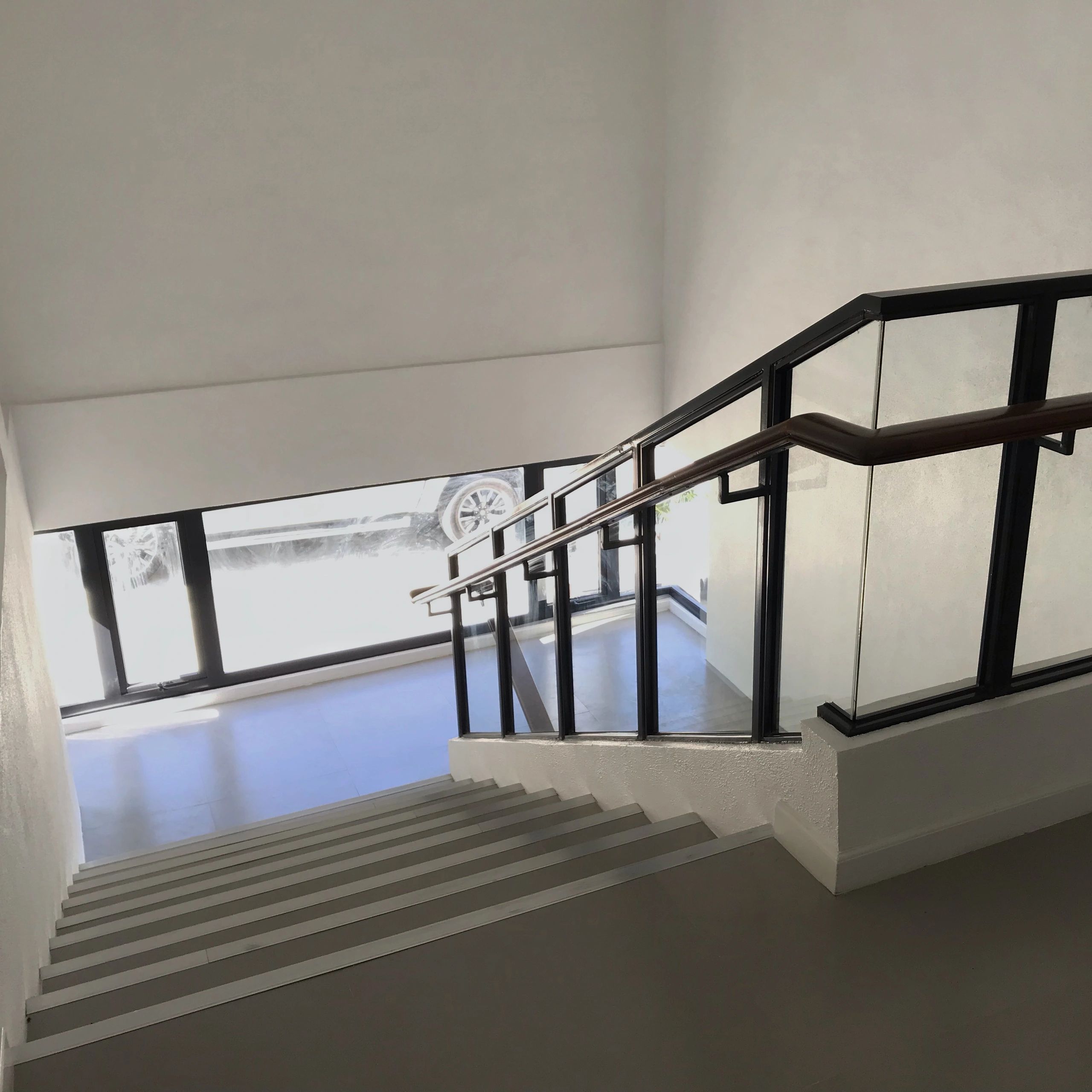 Modern staircase with glass and metal railing overlooking a bright entrance.