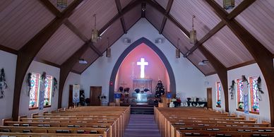 Interior of a church with wooden pews and a glowing cross at the altar.