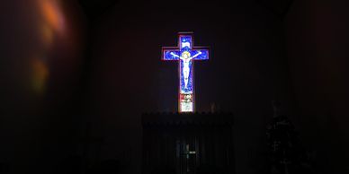 Stained glass cross depicting Jesus illuminated in a dark church.