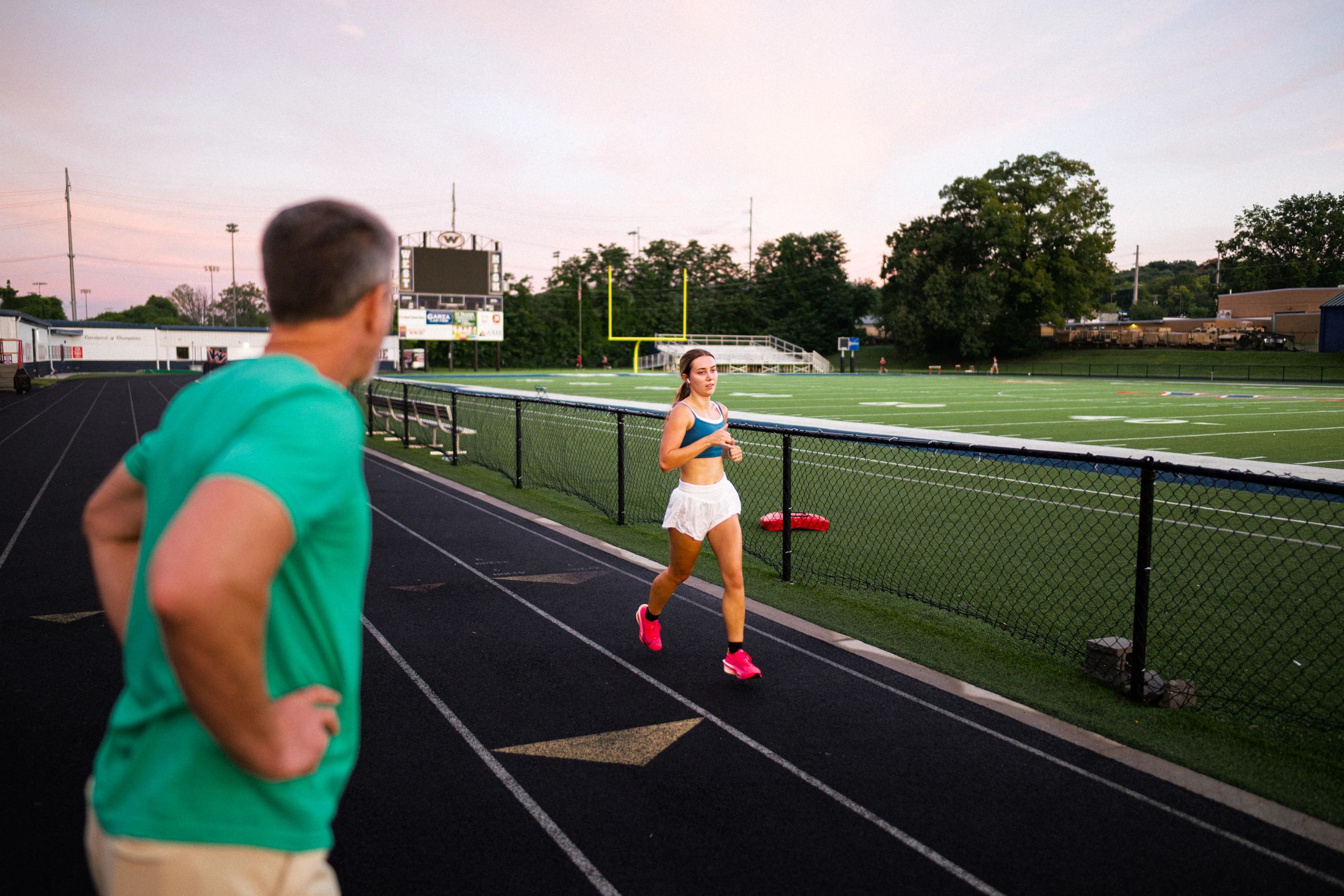 Woman jogging on a track with man watching.