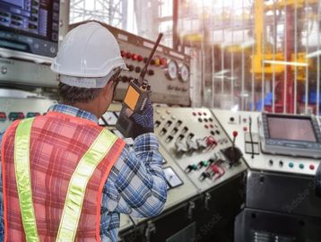 Man in a high visibility vest in a control starion holding a handheld radio