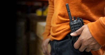close up photo of a walki talki on the hip of a man in a bright orange shirt 
