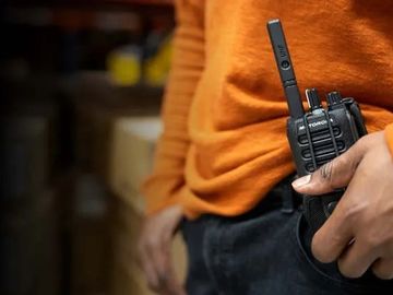 close up photo of a walki talki on the hip of a man in a bright orange shirt 