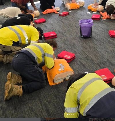 A group of adults kneeling in a circle on the floor, practicing rescue breaths during  CPR training