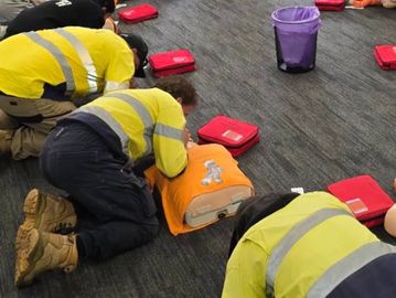 A group of adults kneeling in a circle on the floor, practicing rescue breaths during  CPR training
