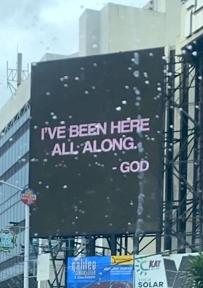 Billboard reads, "I'VE BEEN HERE ALL ALONG. - GOD" in a city setting.