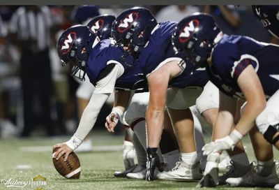 Football players in blue uniforms preparing for a snap on the field.
