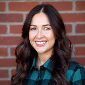 Smiling woman with long wavy hair in front of a brick wall.
