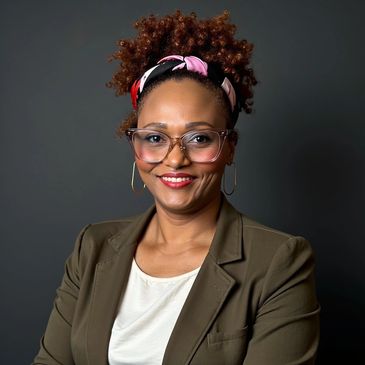 Smiling woman with glasses and headband in a blazer against a dark background.