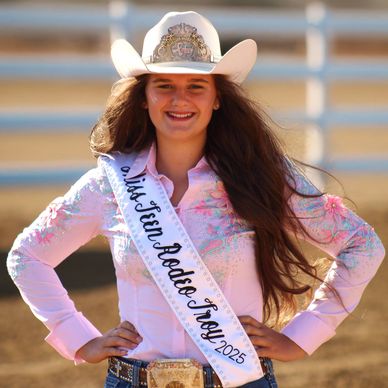 Young rodeo queen wearing a sash and cowboy hat, smiling confidently.