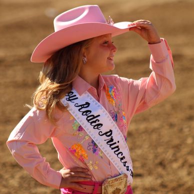 Young rodeo princess in pink outfit and hat at an outdoor event.