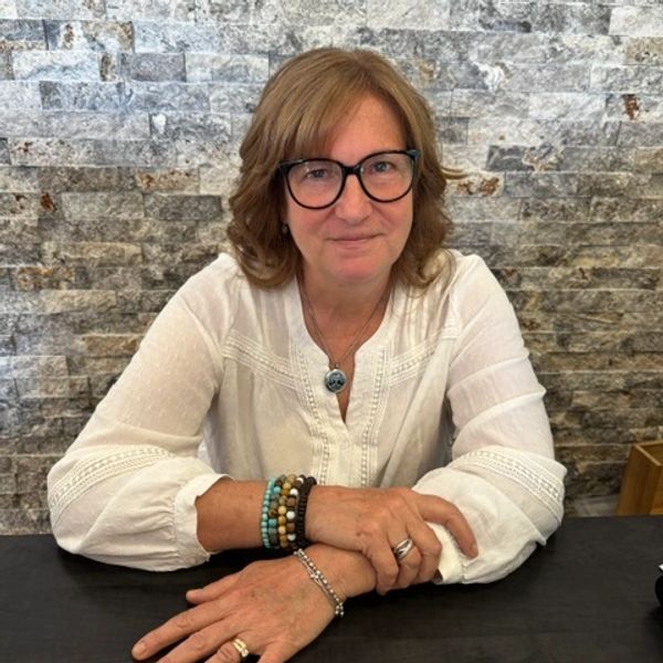 Woman in glasses and white blouse sits at a table with hands folded.