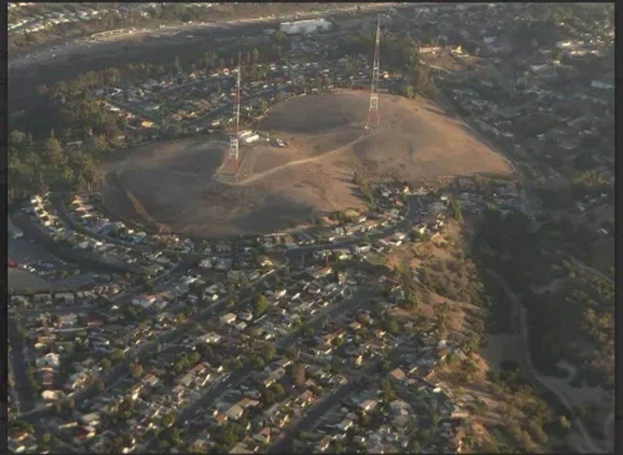 Aerial view of a residential area surrounding a barren hill with communication towers.