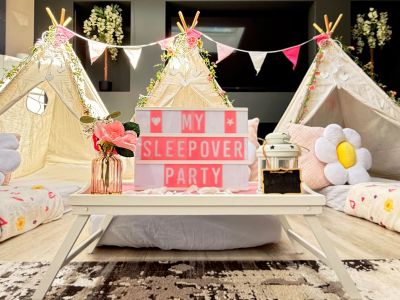 Cozy indoor sleepover setup with tents, cushions, and a sign.