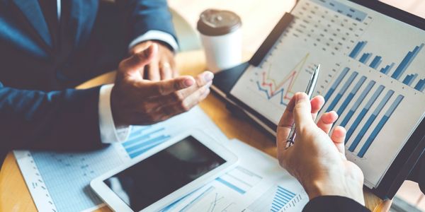 Two professionals discussing financial charts and data on a tablet and paper.