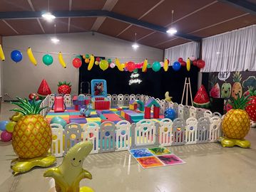 Colorful indoor kids' play area with fruit-themed decorations and soft play mats.
