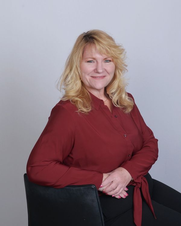 white woman smiling red shirt black pants sitting in chair with arm on rest blonde hair blue eyes