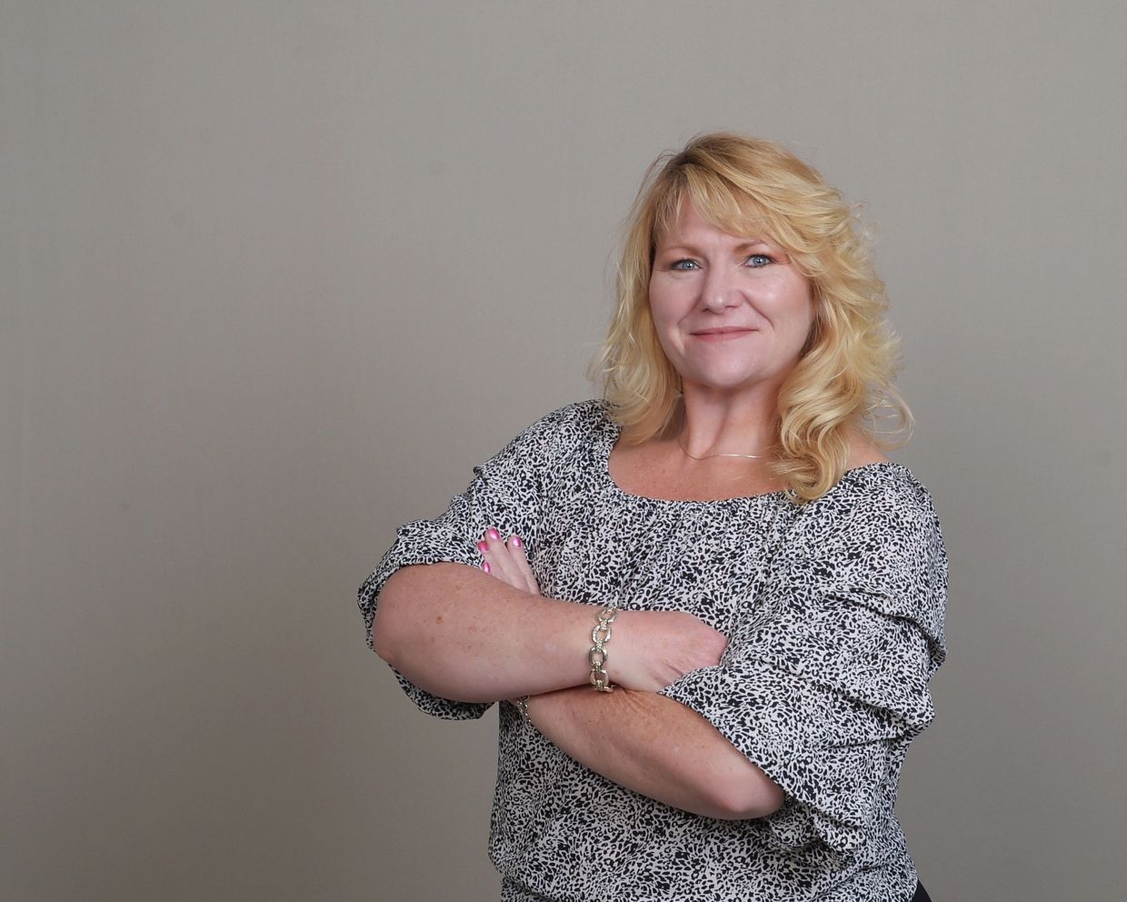 white woman blonde hair blue eyes arms crossed smiling wearing black & white dot shirt standing