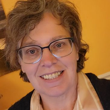Smiling person with glasses and curly hair in a warm indoor setting.
