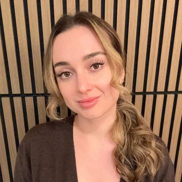 A woman with curled blonde hair posing against a wooden slat wall.