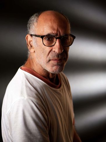 Portrait of a serious elderly man wearing glasses and a white shirt.
