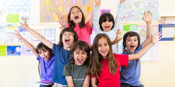 A group of happy children cheering and raising their hands in a classroom.