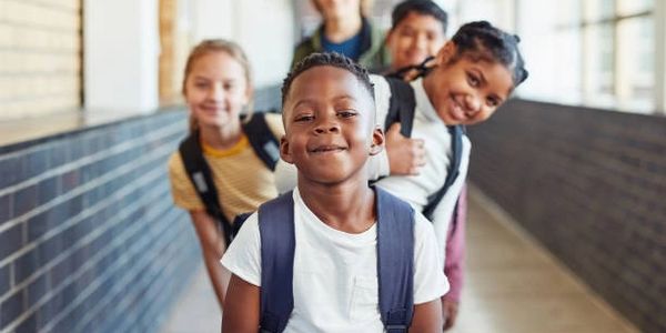 Happy children with backpacks standing in a school hallway.