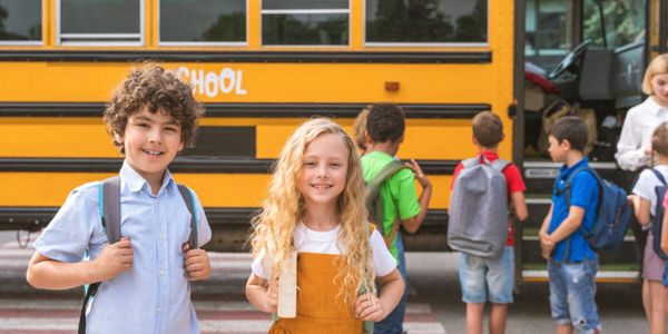 Children with backpacks standing in front of a yellow school bus.