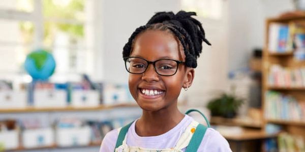 Smiling girl with glasses in a bright classroom.