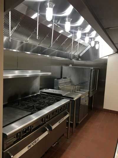 Commercial kitchen with stainless steel appliances and ventilation.