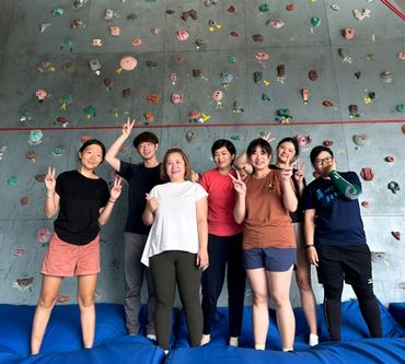 A group of six people posing and smiling in front of a climbing wall.