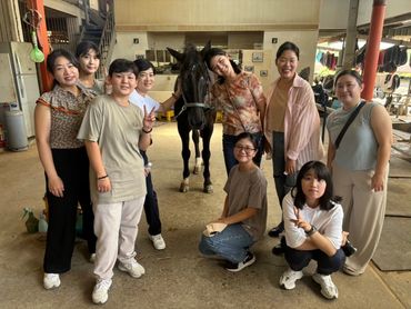 Group of smiling people posing with a horse indoors.