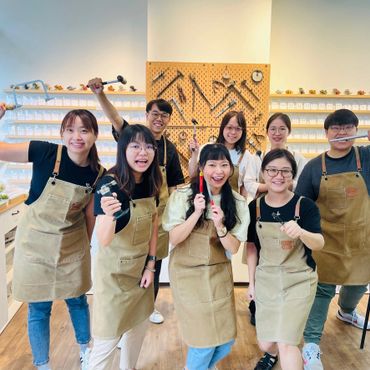 Group of seven smiling people in aprons holding tools in a workshop.