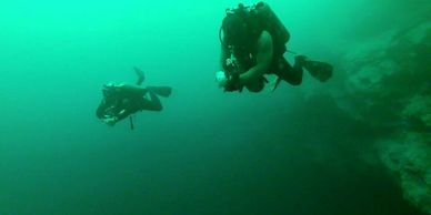 Two scuba divers explore an underwater environment near rocky terrain.