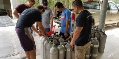 A group of men inspecting scuba tanks indoors near a vehicle.