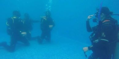Group of scuba divers underwater, one saluting.