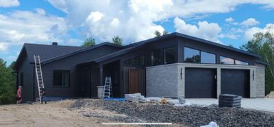 Modern black house with a sloped roof and double garage under construction.