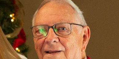 Smiling elderly man wearing glasses and a red sweater.