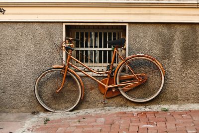 Rusty old bicycle parked against a textured wall with barred window.