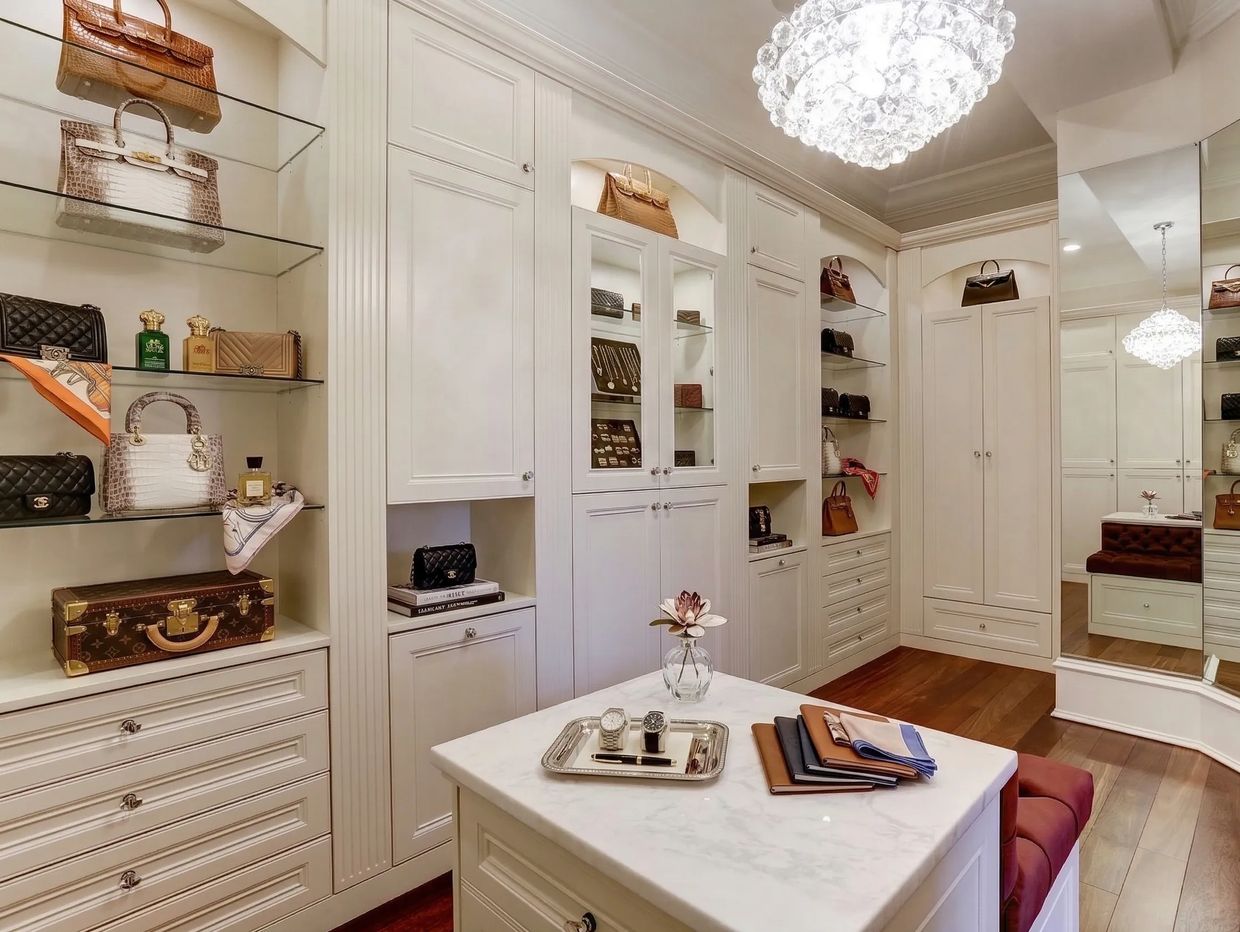 Elegant walk-in closet with white cabinetry, luxury handbags, and a crystal chandelier.