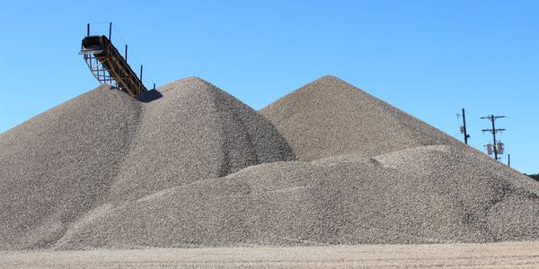 Large piles of gravel with a conveyor belt under a clear blue sky.
