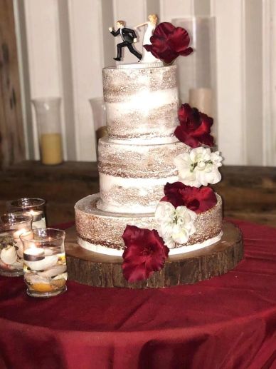 Three-tiered wedding cake with red and white flowers and a humorous bride and groom topper.