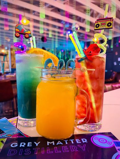 Three colorful cocktails with fun plastic stirrers at a bar.
