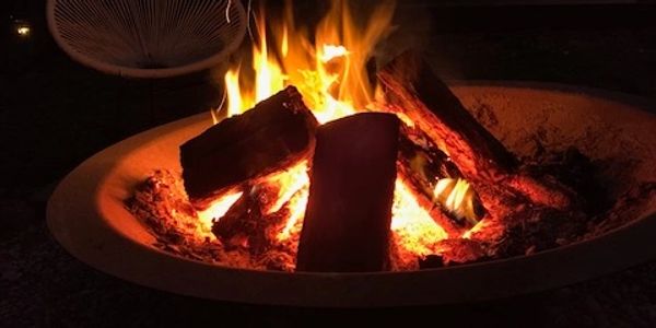 Outdoor fire pit glowing warmly at dusk with a cozy chair nearby.