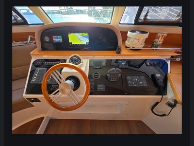 Modern boat helm with wooden steering wheel and digital navigation screens.