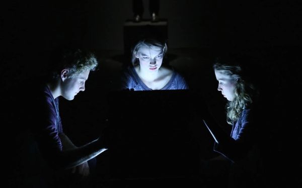 Three people illuminated by a glowing box in the dark.