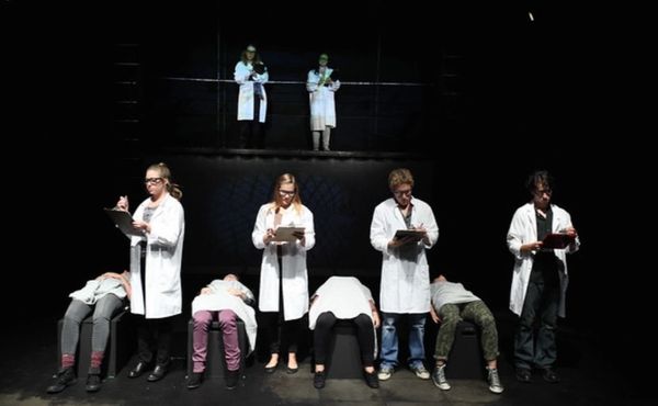 Scientists in lab coats with patients on benches in a dark room.